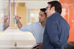 Many writing on white board as another man watches