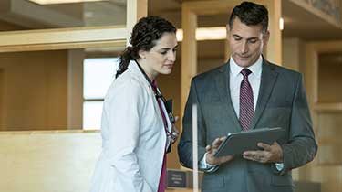 Female doctor looking at male business man's computer tablet